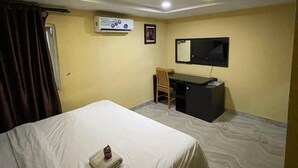 A hotel room with a bed, a desk, a chair, a TV, and an air conditioning unit. - suite 104 (Enugu)