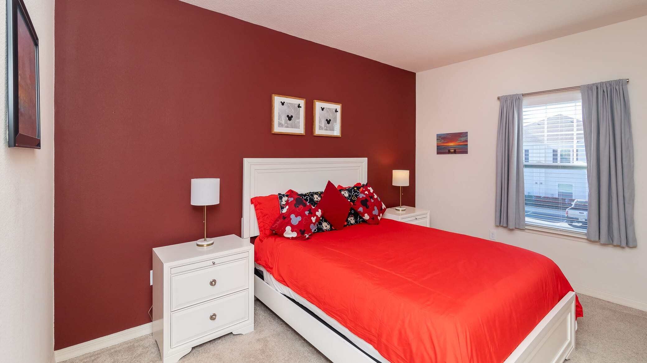 Une chambre avec un mur rouge, un lit blanc, deux tables de chevet et une fenêtre avec des rideaux.