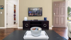 Een woonkamer met een flatscreen-tv waarop 'Mandaloriaan' te zien is, een donker houten salontafel met een dienblad en een schaal met snacks, een donkere tv-meubel en een beige muur.