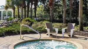 Un jacuzzi rodeado de sillones de descanso y una zona junto a la piscina con un camino de ladrillo.