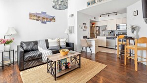 A modern living room with a black leather sofa, a coffee table with books, and a kitchen area with white cabinets and a dining table. - Adventure's at Villa Del Sol (Kissimmee)