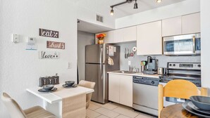 A modern kitchen with white cabinets, stainless steel appliances, and a dining area with a white table and chairs. - Adventure's at Villa Del Sol (Kissimmee)