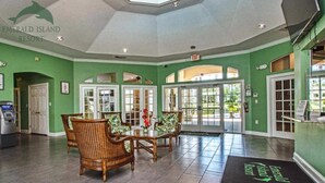 A lobby with a reception desk, a seating area with wicker chairs, and a large glass door leading outside. - Be Our Guest at Emerald Island (Kissimmee)