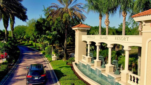 A road leading to a resort entrance with a sign reading "EMERALD ISLAND RESORT". - Be Our Guest at Emerald Island (Kissimmee)