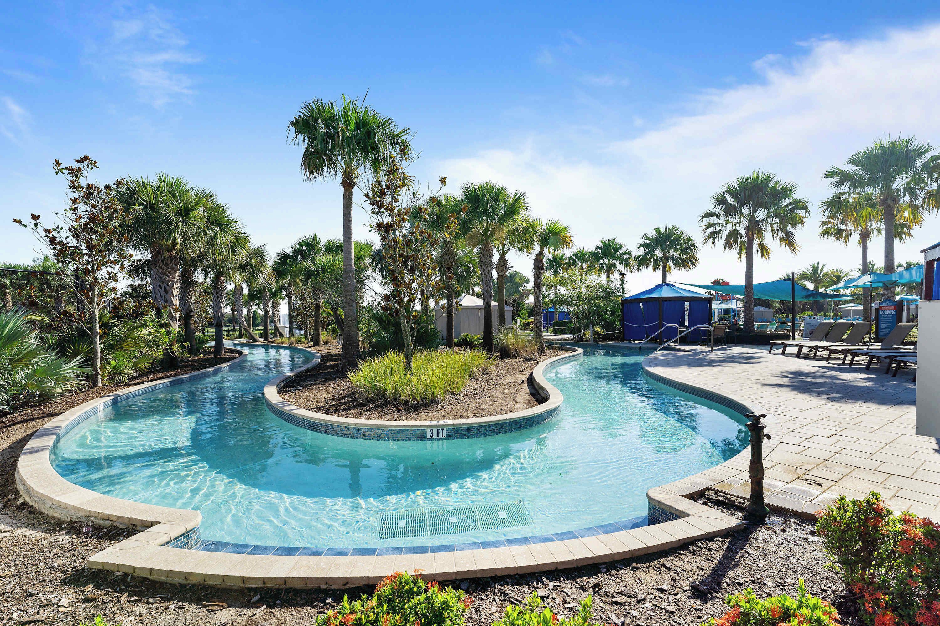 A swimming pool with a curved design, surrounded by palm trees and lounge chairs.