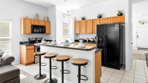 A modern kitchen with wooden cabinets, a black refrigerator, a microwave, and a bar area with stools.