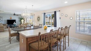 A spacious dining area with a large island table, surrounded by wicker chairs, and a chandelier. - Magic Oasis Retreat (Davenport)