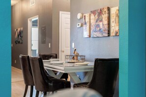 Un comedor con una mesa dispuesta para cuatro personas, sillas de cuero negro y una pared decorada con arte abstracto.