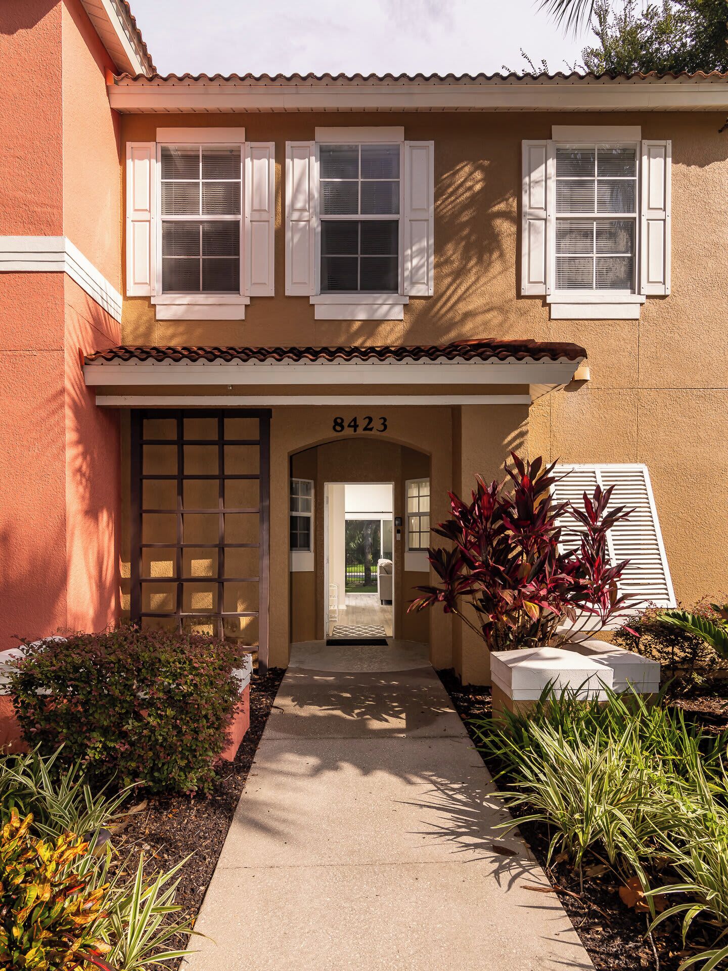 A two-story building with a beige facade, numbered 8423, featuring a front entrance with a glass door, a small porch, and a pathway leading to the door.