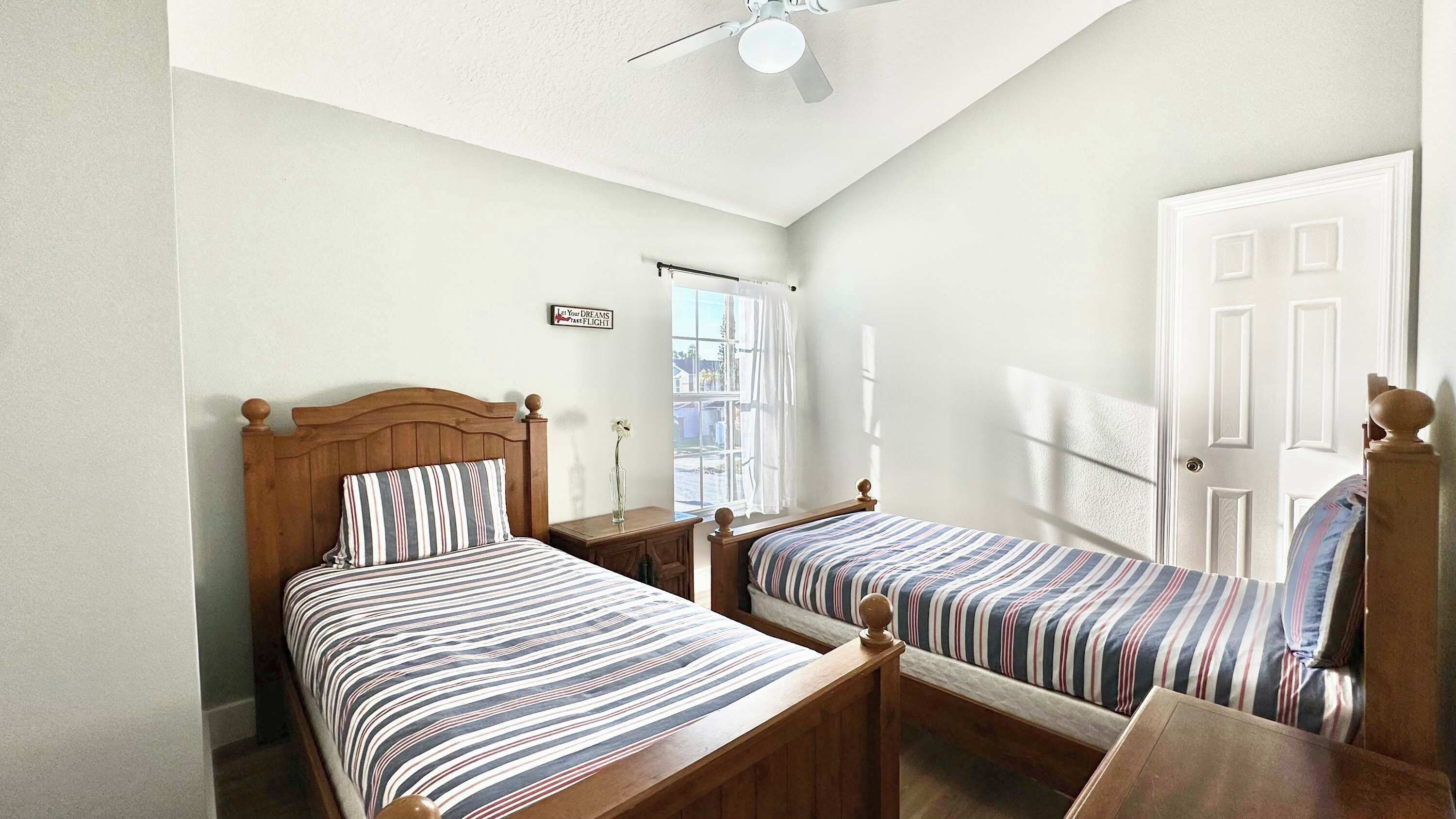 A bedroom with two wooden beds, a ceiling fan, a window with a view, and a door.