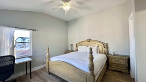 A bedroom with a bed, a desk, a chair, a nightstand, a bedside table, and a ceiling fan.