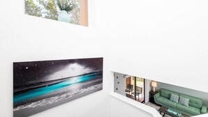 Un interior moderno con un mural grande en la pared que muestra una playa de noche, un sofá verde y vistas a un balcón con mobiliario exterior.