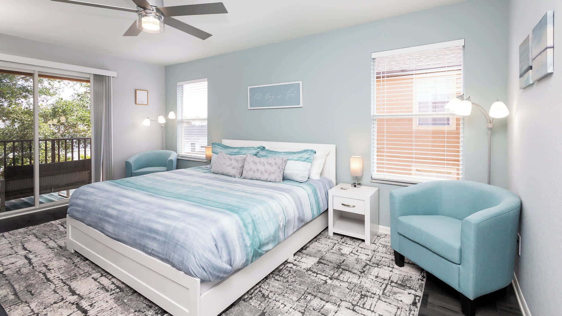 A bedroom with a bed, two chairs, a nightstand, and a ceiling fan.