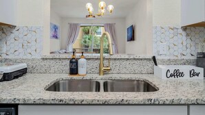 A kitchen with a granite countertop, a stainless steel sink, a gold faucet, and a sign labeled "Coffee Bar".