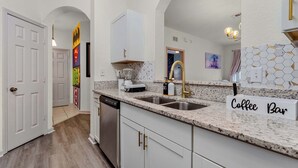 A modern kitchen with white cabinetry, granite countertops, and a coffee bar sign.