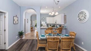 A dining area with wicker chairs, a table set with blue plates, and a wall clock.