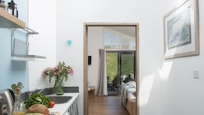 Una cocina con tabla de cortar, verduras y una botella de aceite. Hay una cama con vistas al exterior.