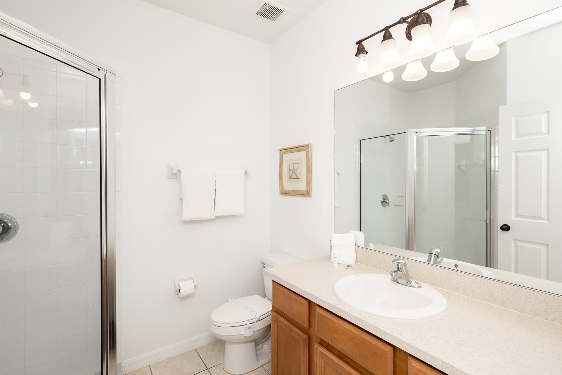 A modern bathroom with a glass shower enclosure, a white toilet, a sink with a mirror above, and a light fixture above the mirror.