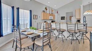 Una cocina moderna con armarios de madera, un microondas y un comedor con sillas de metal y una mesa preparada para cuatro.