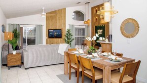 A modern living room with a sofa, dining table set for four, and a TV mounted on the wall. - Jewel of Emerald Island with Heated Pool! (Kissimmee)