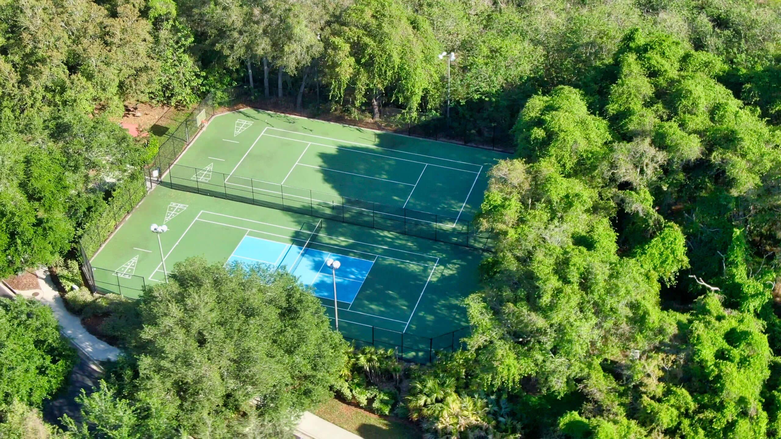 An aerial view of a tennis court surrounded by dense greenery.
