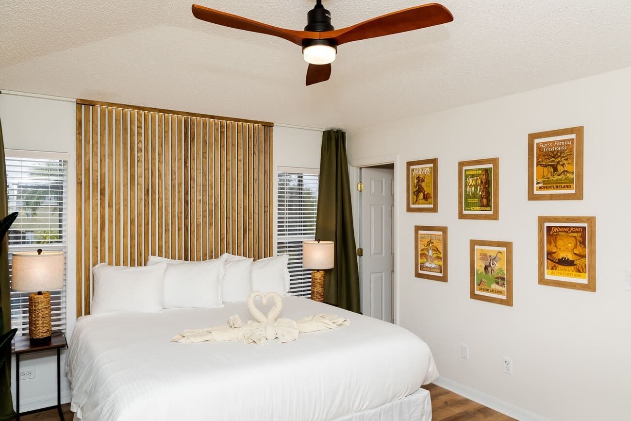 Una habitación de hotel con una cama grande, un ventilador de techo, un panel de pared de listones de madera y carteles enmarcados.