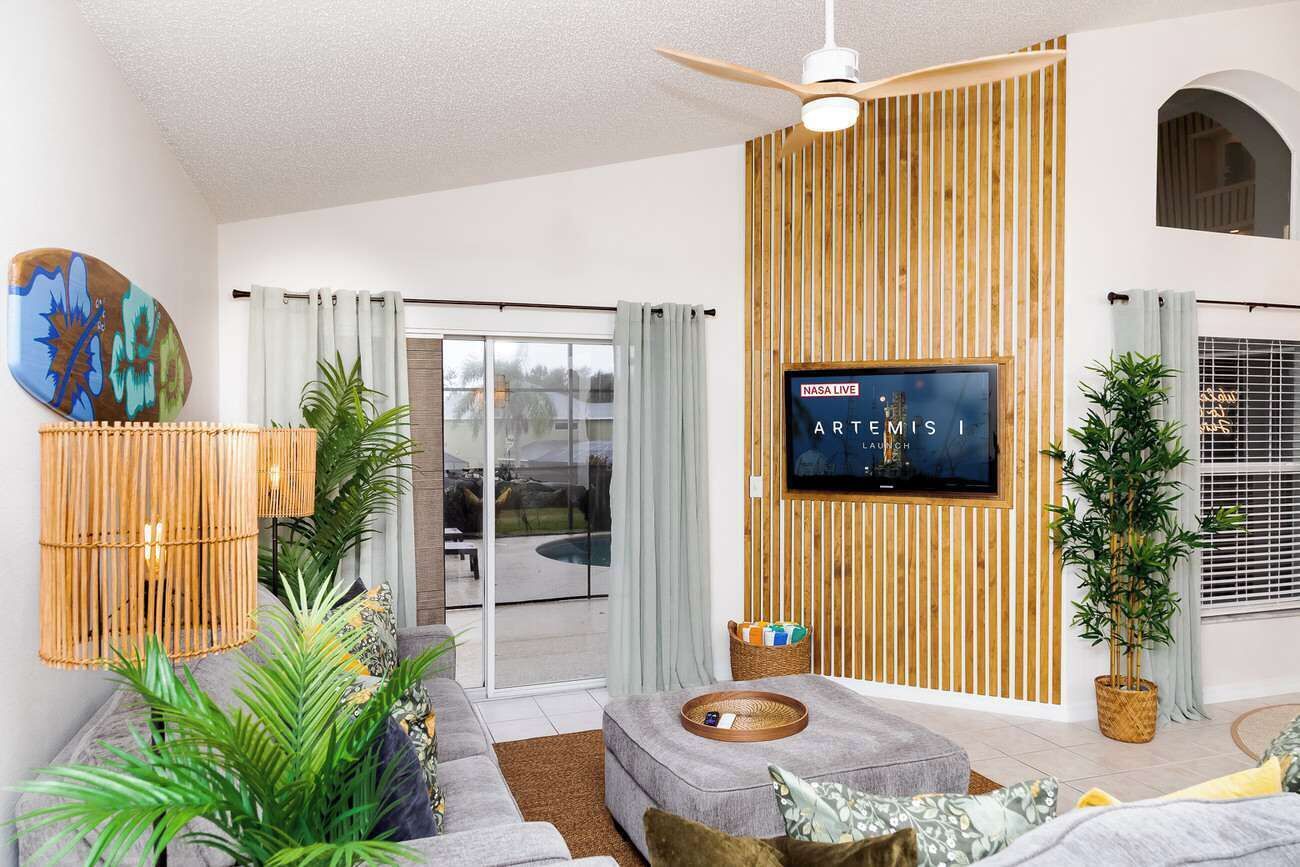 A modern living room with a sofa, a television mounted on a wooden wall, and a ceiling fan.