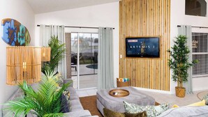 A modern living room with a sofa, a television mounted on a wooden wall, and a ceiling fan. - Jewel of Emerald Island with Heated Pool! (Kissimmee)