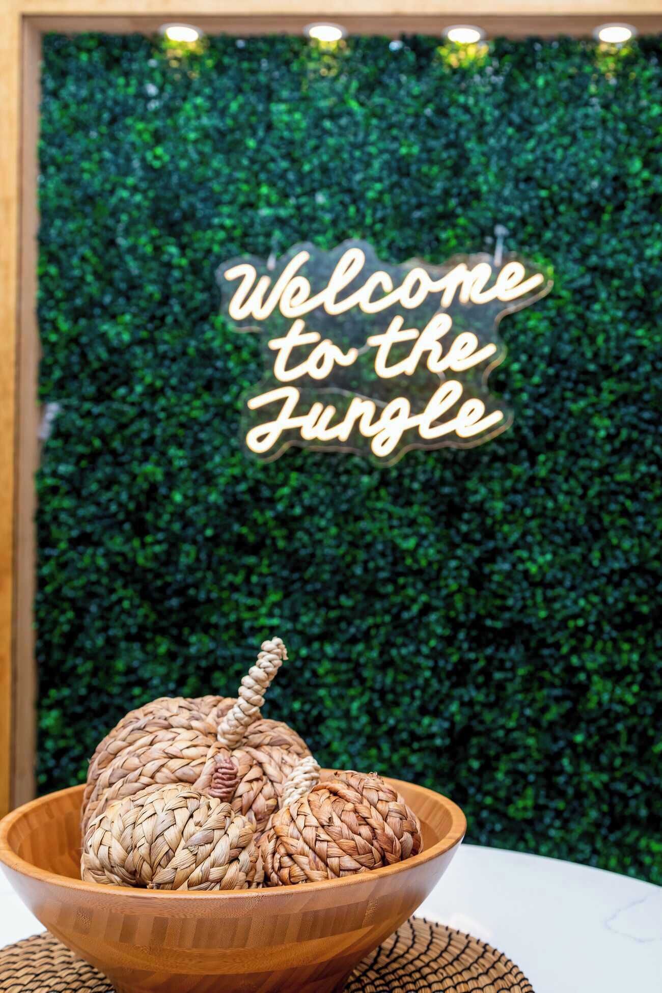 A welcome sign and a woven basket on a table against a green wall.