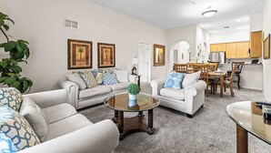 A spacious living room with a sofa set, a coffee table, and a dining area with wooden chairs and a table. - Slice Of Sunshine At Caribe Cove (Kissimmee)