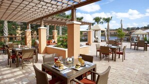 An outdoor patio area with wicker furniture, tables with drinks, and a view of the sea.
