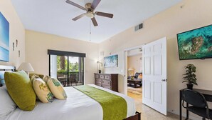 Un dormitorio con cama, escritorio, ventilador de techo, televisor y vista al exterior.