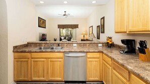 A kitchen with wooden cabinets, a dishwasher, a coffee maker, and a window with a view of the outdoors.