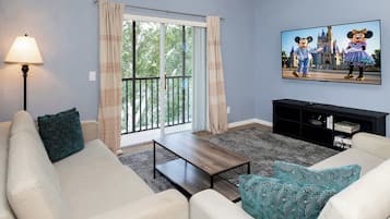 A living room with a sofa, a coffee table, a lamp, a TV, and a painting of Disney characters.
