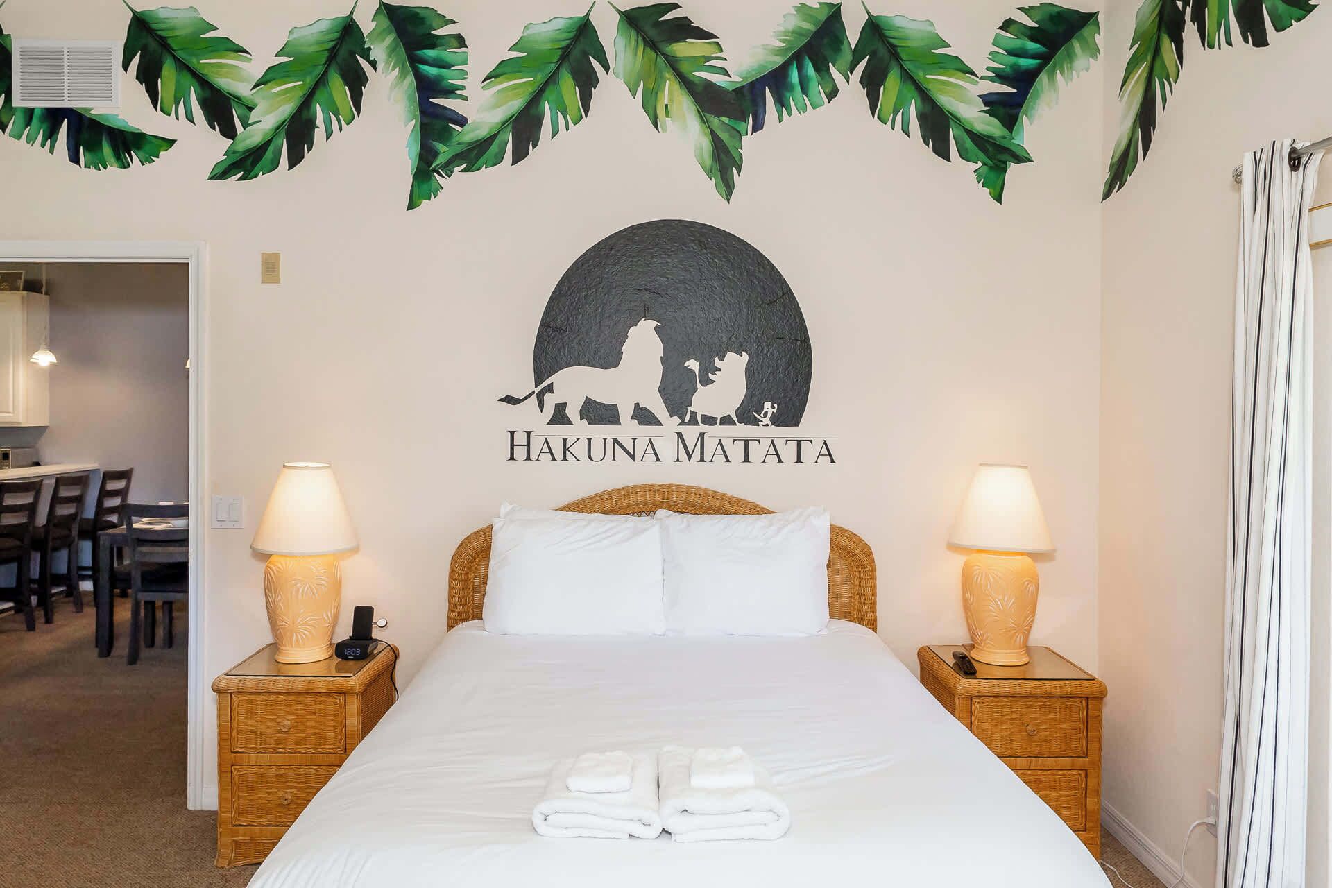 A hotel room with a bed, two bedside lamps, a wall-mounted artwork of a lion and a pig, and a tropical leaf decoration above the artwork.