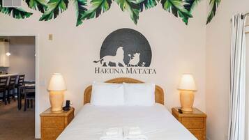 A hotel room with a bed, two bedside lamps, a wall-mounted artwork of a lion and a pig, and a tropical leaf decoration above the artwork.