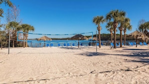 Una cancha de voleibol de playa con red azul, palmeras y sillas.