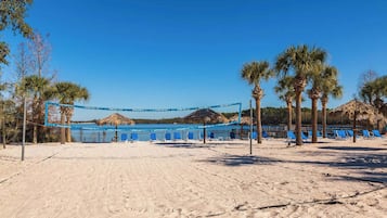 A beach volleyball court with blue netting, palm trees, and beach chairs.