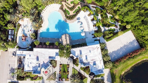 Luchtbeeld van een resort met een groot zwembad, meerdere gastenkamers en weelderige beplanting.