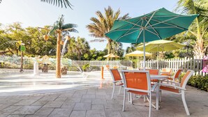 Een buitenruimte met tafels, stoelen, parasols en een witte schutting.
