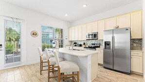 A modern kitchen with white cabinetry, stainless steel appliances, and a central island with bar stools. - Parrot Paradise Escape for 8! (Kissimmee)