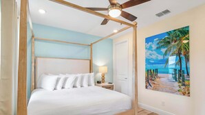 A four-poster bed with white linens, a wooden headboard, a nightstand with a lamp, and a beach-themed painting on the wall. - Turquoise Breeze - Close to Disney (Kissimmee)