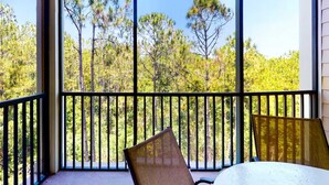 Un balcón con vistas a un bosque, una mesa y dos sillas.