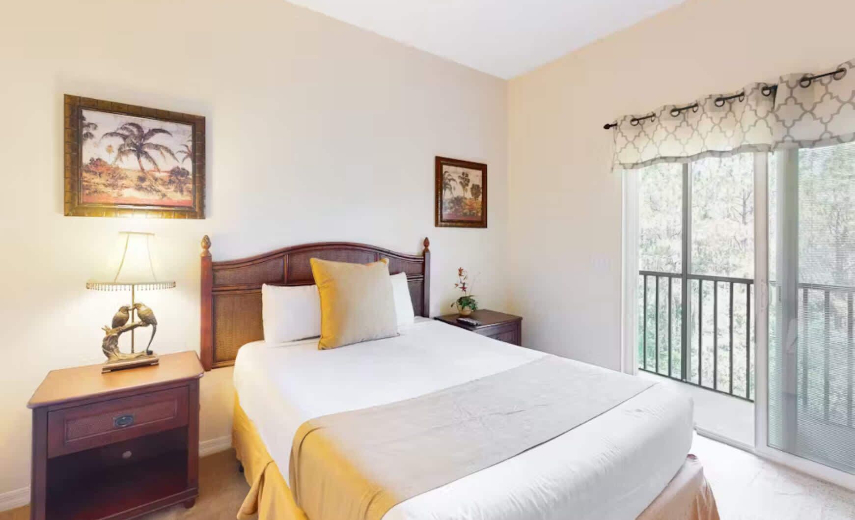 Une chambre à coucher bien rangée, avec un grand lit, deux tables de chevet, une lampe et des tableaux encadrés accrochés aux murs.