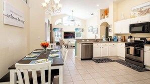 A spacious kitchen with white cabinets, a central island, and a dining area with a table set for four. - Beachy Retreat (Kissimmee)