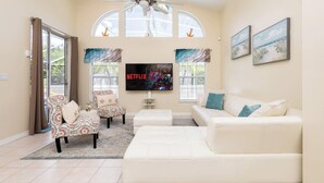A spacious living room with a large TV, comfortable seating, and large windows. - Beachy Retreat (Kissimmee)
