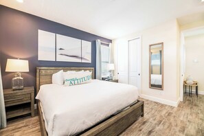 A bedroom with a large bed, a nightstand with a lamp, a dresser, and a mirror on the wall.