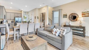 A modern living room with a grey sofa, wooden coffee table, and a dining area with a table and chairs.