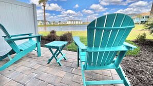 A patio with turquoise Adirondack chairs and a small table, overlooking a body of water and buildings in the background. - Sunkissed at Margaritaville - Serene Lake Views (Kissimmee)
