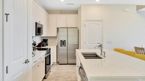 A modern kitchen with white cabinets, stainless steel appliances, and a large island with a sink. - Sunkissed at Margaritaville - Serene Lake Views (Kissimmee)